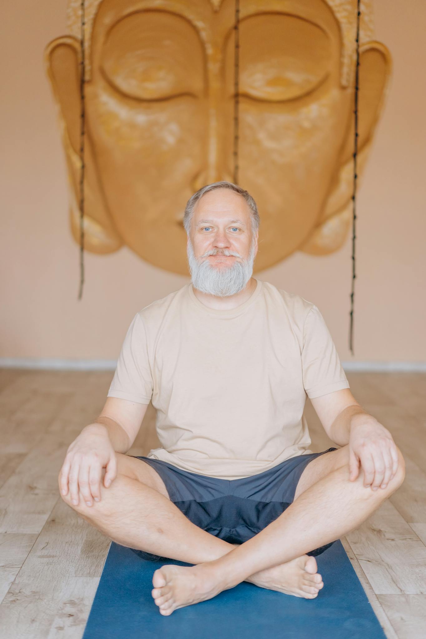 A serene senior man in yoga position in a tranquil studio with a Buddha backdrop.