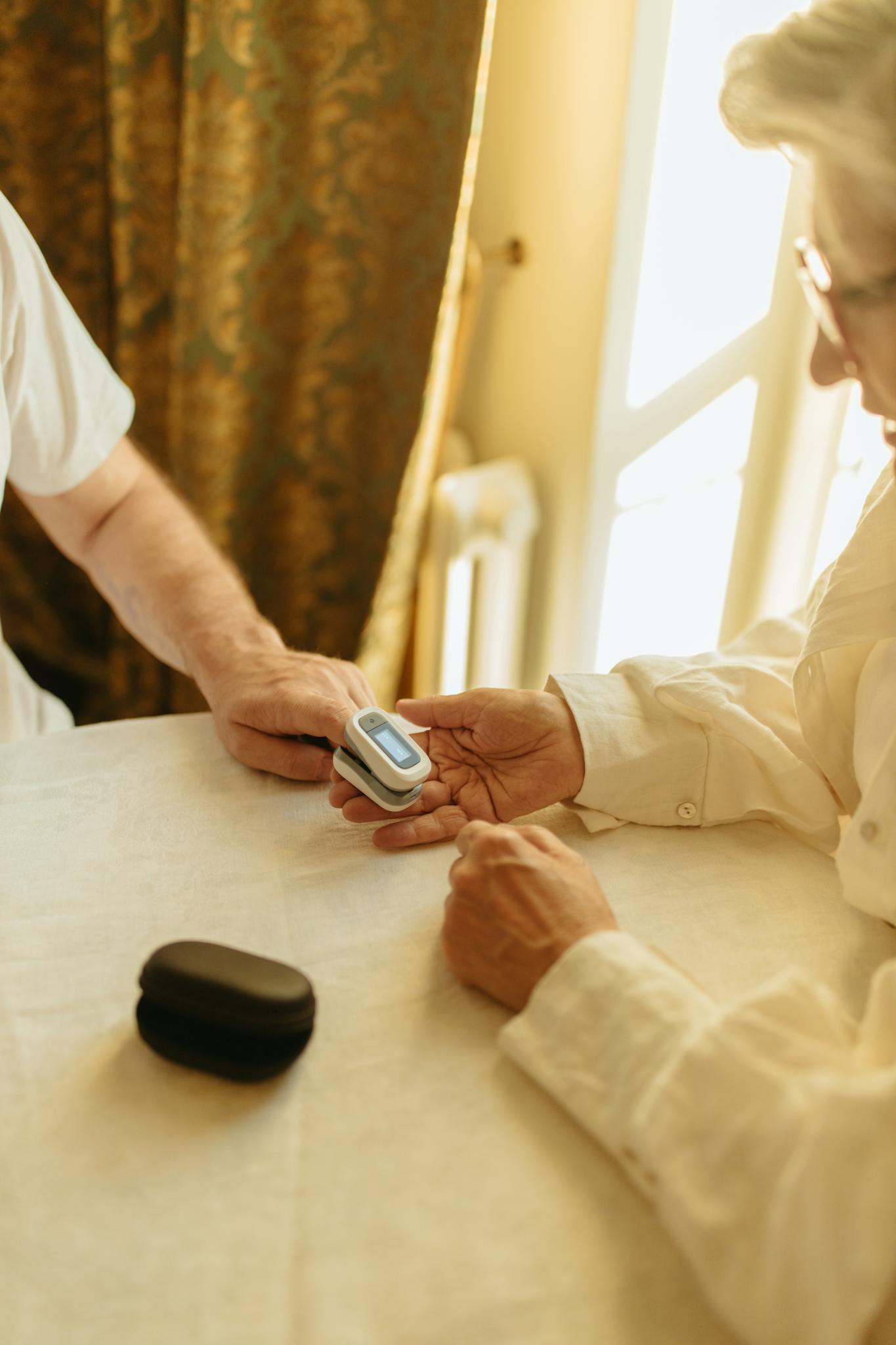 Elderly person using a pulse oximeter indoors for health monitoring.
